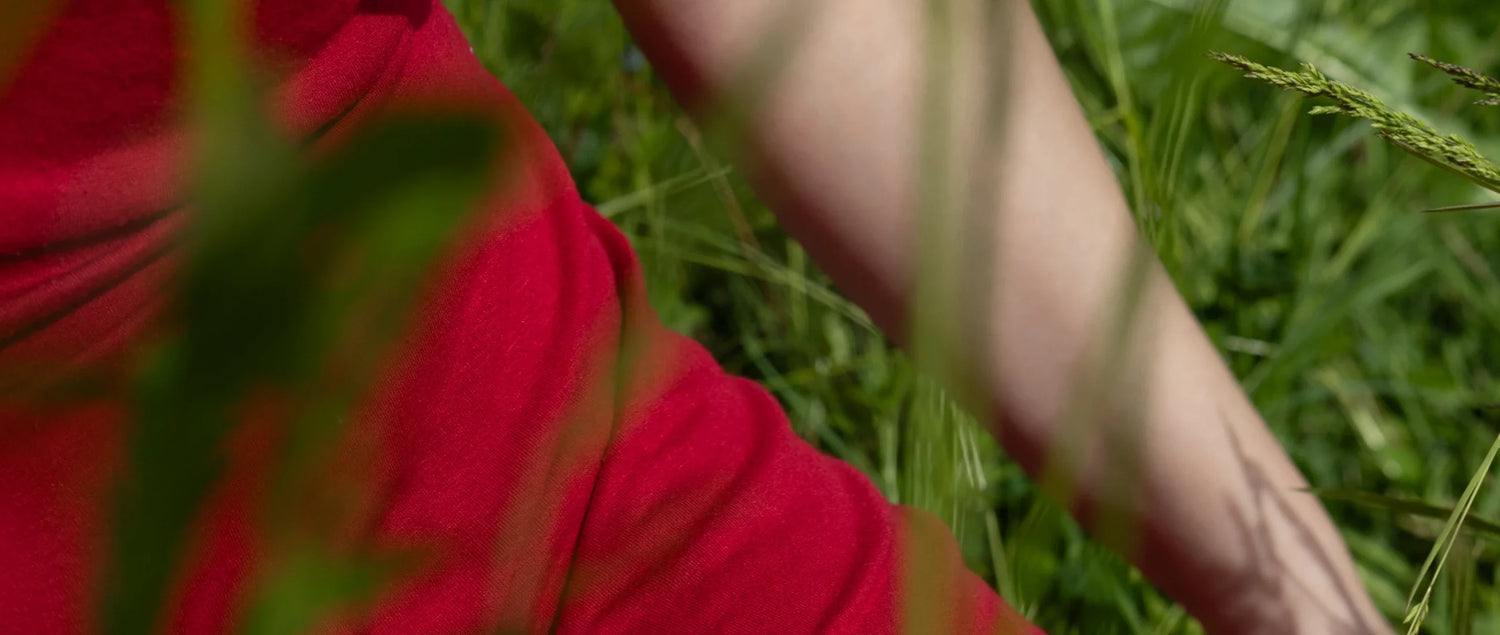 Détail d'une robe rouge portée par une femme assise dans l'herbe